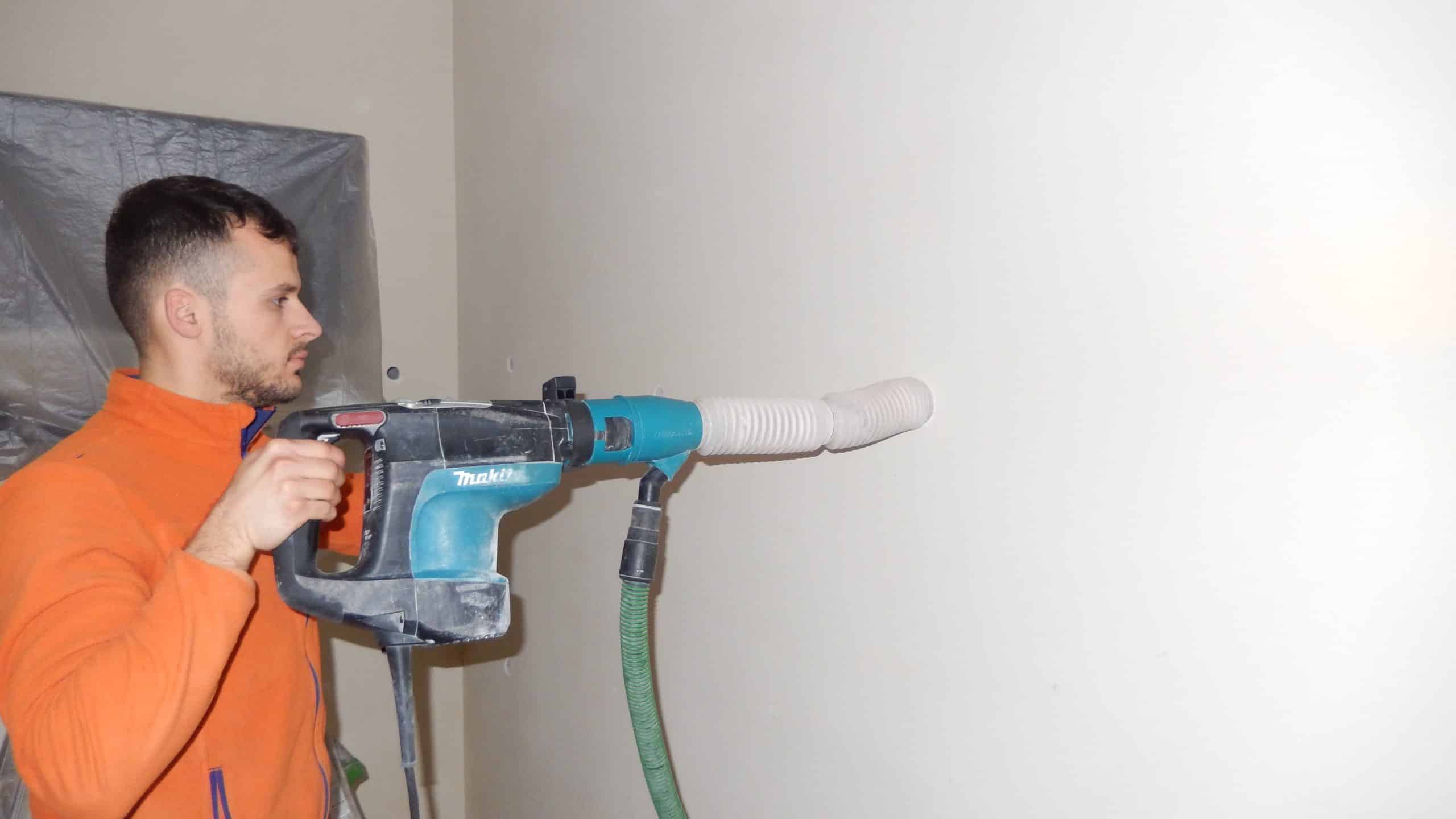 Persona che fora una parete con trapano Makita e sistema di aspirazione.
