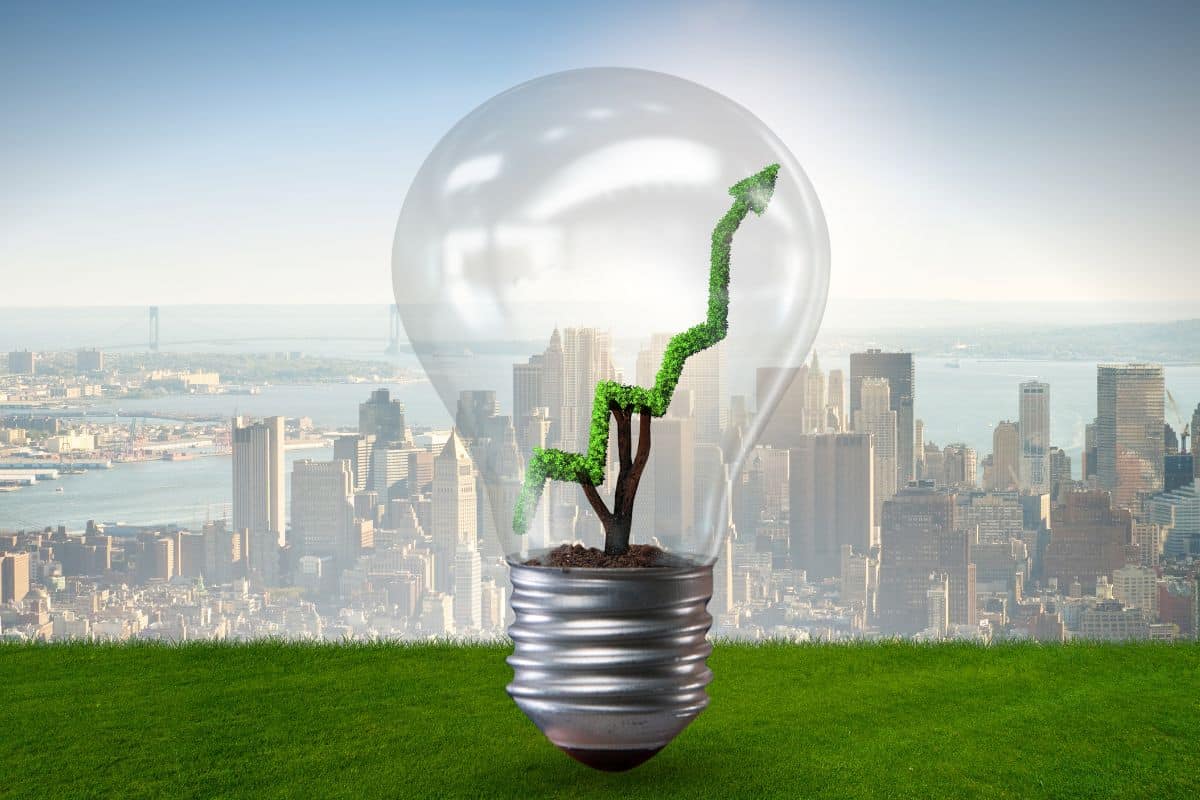 Lampadina con pianta e freccia verde su sfondo città: energia pulita.