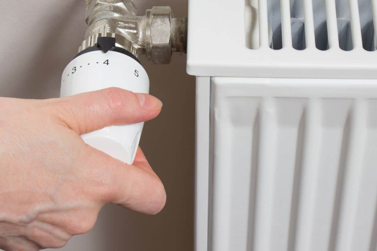 Mano che regola una valvola di un termosifone bianco in casa.
