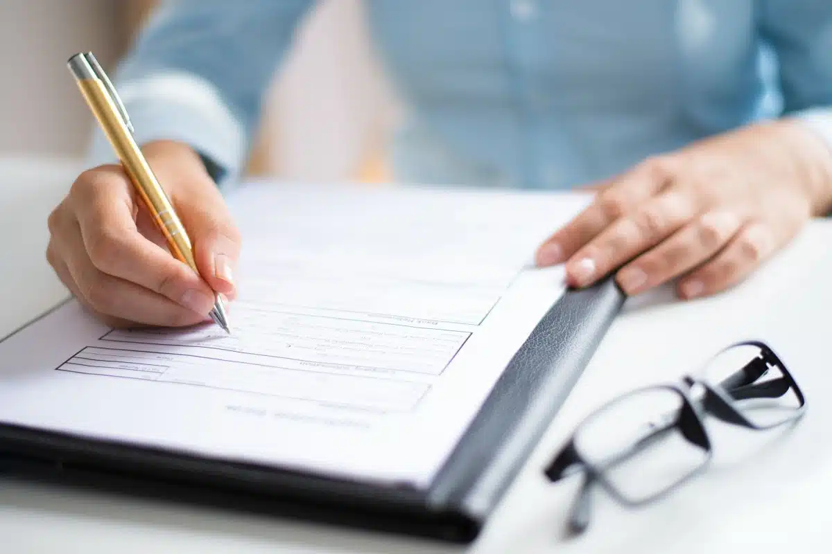 Certificazione APE: mano firma documento energetico, occhiali accanto.