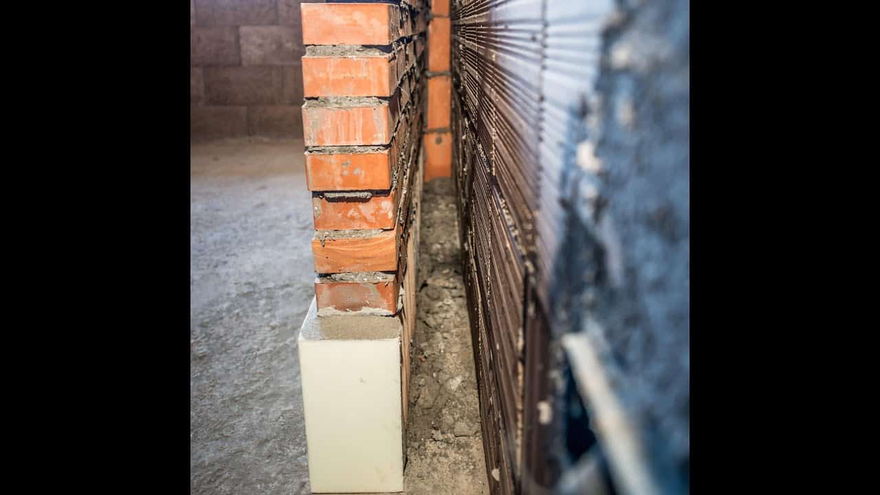 Muro di mattoni rossi in costruzione, spazio tra le pareti. Isolamento termico bianco alla base.