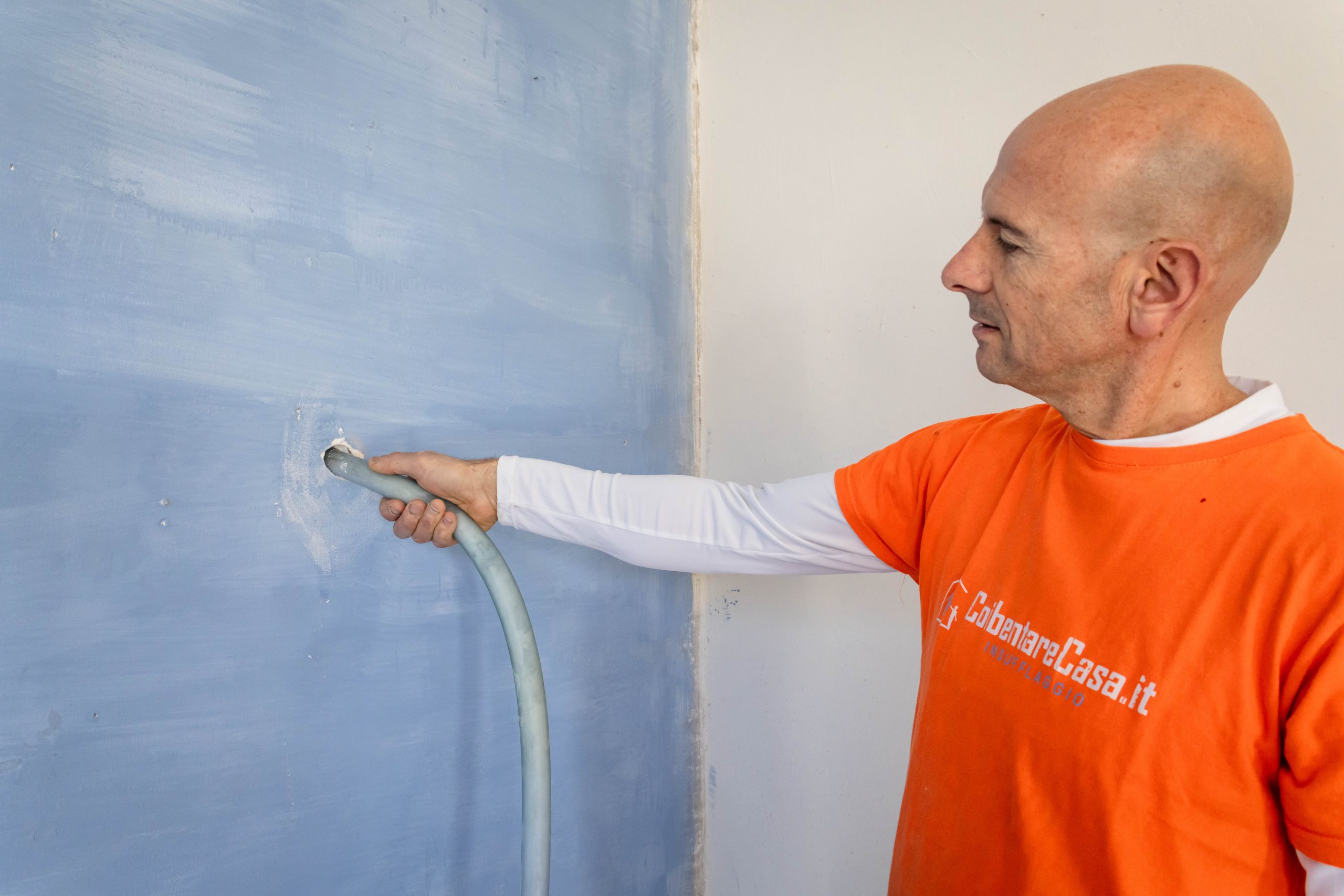 Isolamento termico casa 2025: uomo che applica coibentazione a parete con tubo. Offerta speciale per coibentare la tua casa.