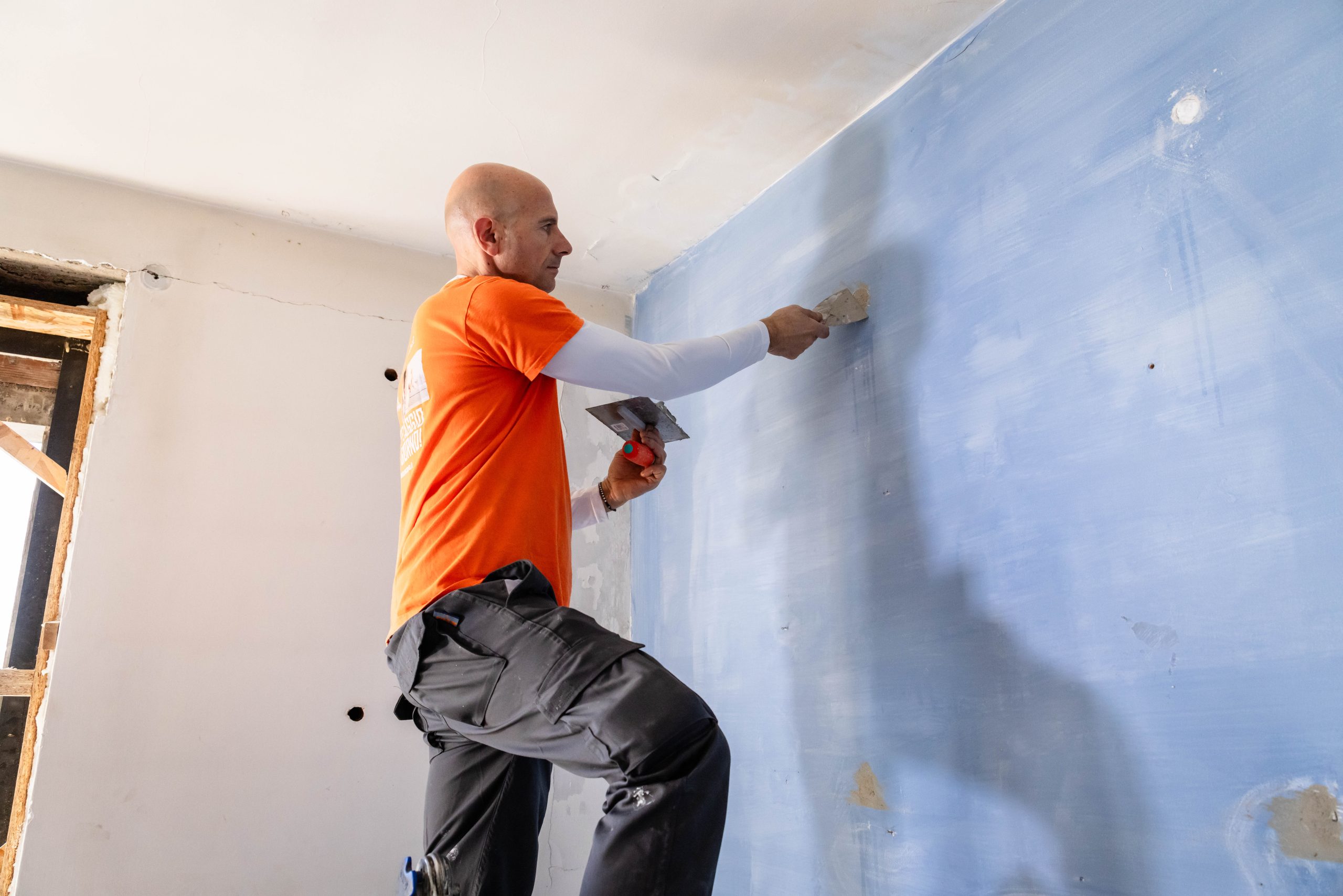 Operaio edile che stucca parete azzurra. Ristrutturazione casa, imbianchino professionista con spatola. Lavori interni, finitura pareti.