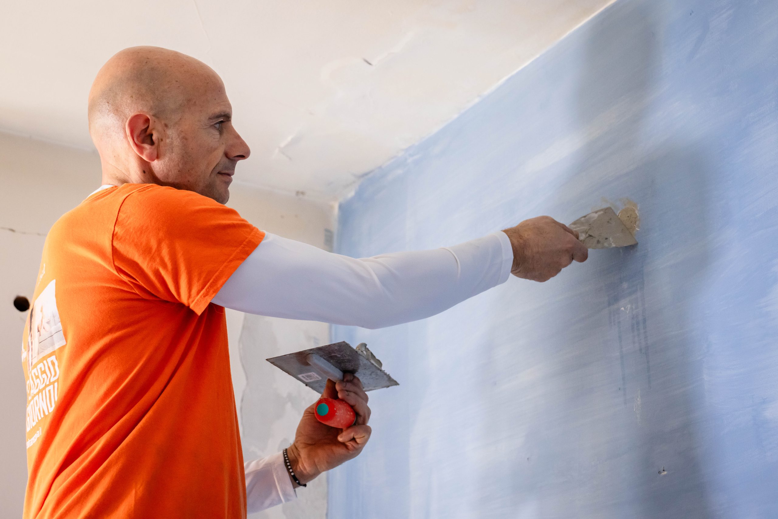 Imbianchino professionista che stucca una parete azzurra. Ristrutturazione casa, imbiancatura interni. Lavori di edilizia.